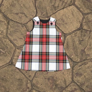 Puede incluir: Un vestido sin mangas de cuadros blancos, rojos y negros con cuello negro y dos botones negros.