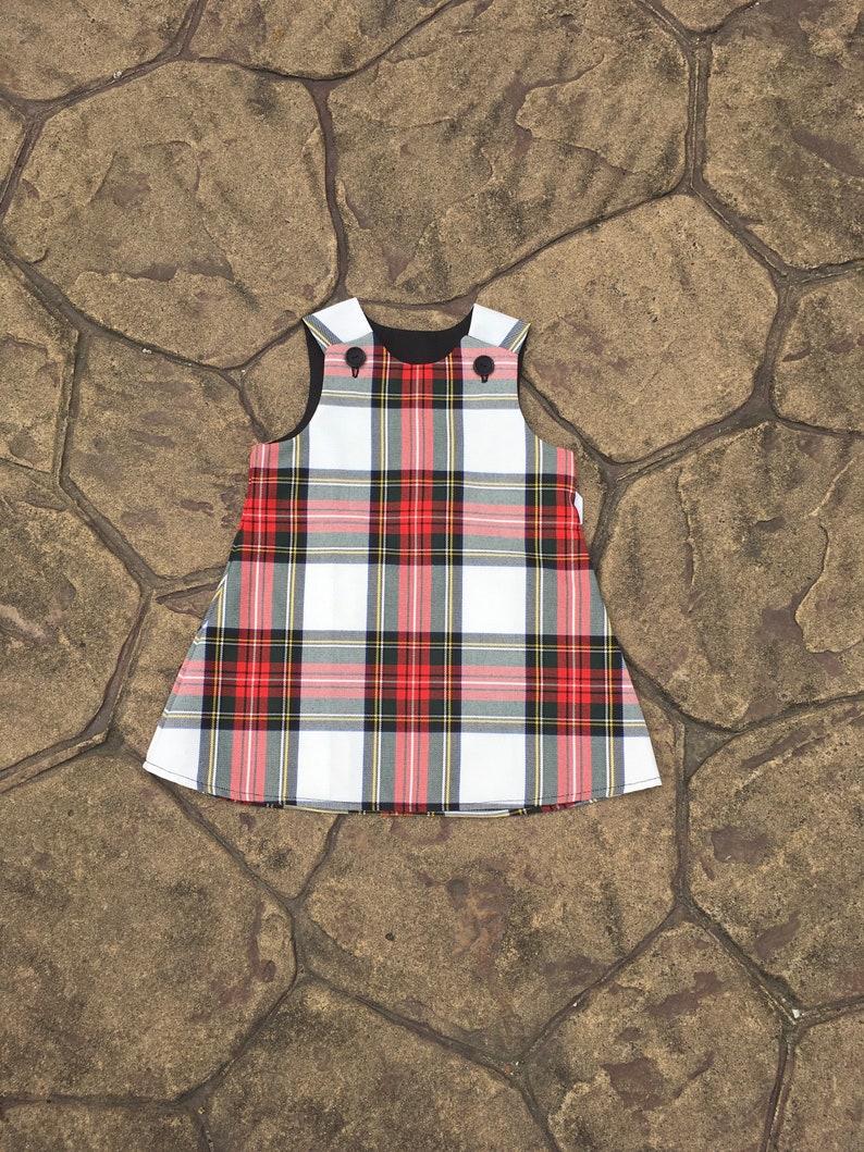 Puede incluir: Un vestido sin mangas de cuadros blancos, rojos y negros con cuello negro y dos botones negros.