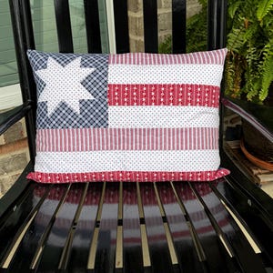 May include: A rectangular throw pillow featuring a patchwork design with a white eight-pointed star on a navy blue plaid background. The pillow includes horizontal stripes of red and white polka dots, red and white stripes, and red floral patterns.