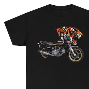May include: Black t-shirt featuring a graphic of a motorcycle and a tiger's head. The motorcycle is a Ducati 325.