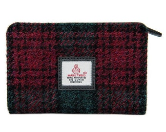 Könnte beinhalten: Eine kleine, rote und grüne Tweed-Reißverschlusstasche mit einem schwarzen Leder-Reißverschluss. Die Tasche hat ein weißes Etikett mit dem Text "HARRIS TWEED HAND WOVEN IN THE OUTER HEBRIDES" in Schwarz.