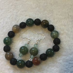 May include: A bracelet and earrings set made with green, brown, and black beads. The bracelet is made with lava rock and agate beads. The earrings are made with green agate beads.