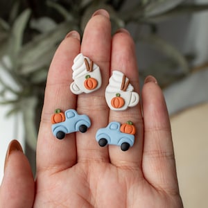 May include: A set of four polymer clay earrings featuring fall-themed designs. Two earrings are white with a brown swirl and a small orange pumpkin. The other two earrings are blue with a white truck bed and a small orange pumpkin.