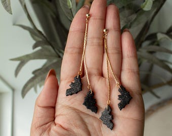 Op de afbeelding: Drie paar oorhangers met zwarte glitter-vleermuisbedels die aan gouden kettingen hangen.