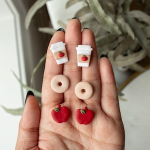 May include: A set of six polymer clay earrings featuring a coffee cup with an apple, a donut, and a red apple.