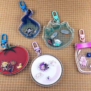 以下が含まれることがあります： カラフルなデザインの透明アクリルキーホルダー5個セット。キーホルダーは、トマト、瓶、炎など、さまざまな形をしており、それぞれに金属製の留め金が付いています。キーホルダーには、小さくカラフルなキャラクターイラストが含まれています。