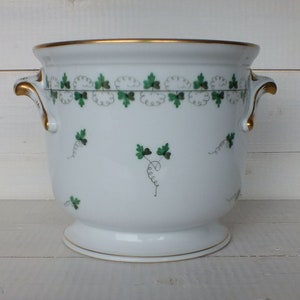 Puede incluir: Cubo de hielo de porcelana blanca con ribete dorado y diseño de hojas verdes. El cubo tiene dos asas.