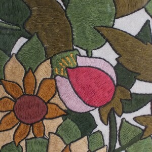 May include: Embroidered floral design featuring pink, red, brown, and blue flowers on a white background. The flowers are surrounded by green leaves.