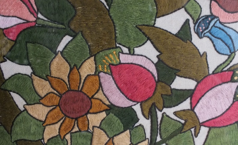 May include: Embroidered floral design featuring pink, red, brown, and blue flowers on a white background. The flowers are surrounded by green leaves.