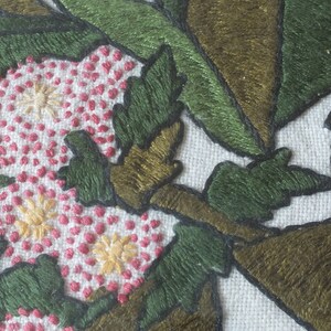 May include: Close-up of embroidered fabric with pink, white and yellow flowers, green leaves and brown branches.