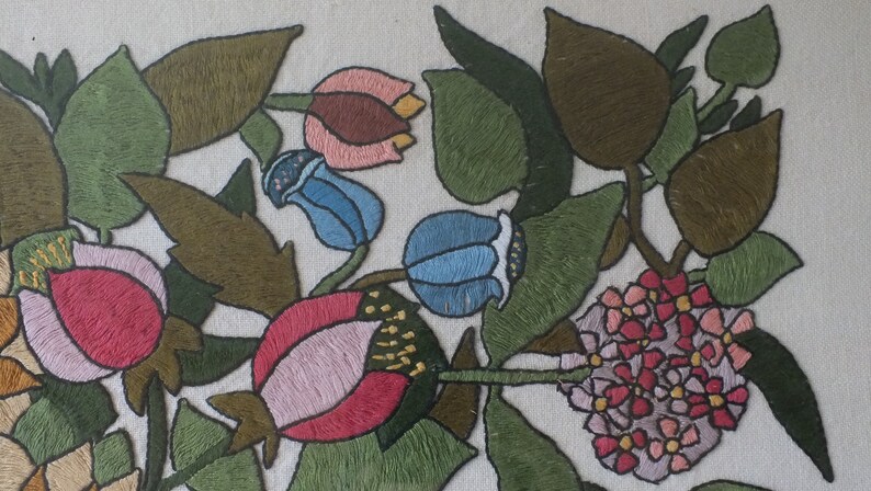 May include: Embroidered floral design featuring pink, red, blue, and green flowers on a white background. The flowers are surrounded by green leaves.