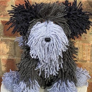 May include: A fluffy gray and black yarn dog toy with a long, shaggy coat. The toy has a black nose and brown eyes.