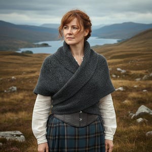 Op de afbeelding: Een vrouw draagt een grijze gebreide sjaal, een witte blouse en een blauw-groene geruite rok. Ze draagt ook een donkerbruin korset. De achtergrond toont een landschap met bergen en een meer.