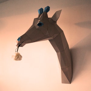 May include: A gray papercraft giraffe head with blue accents, holding a white flower in its mouth.