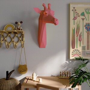 May include: A pink origami giraffe head mounted on a light gray wall, a wooden table with a small teapot and a cup, a wicker basket, a small wooden toy, and a potted plant with green leaves.