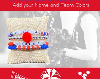 Peut inclure: Un ensemble de bracelets de cheerleading avec des perles rouges, blanches et bleues. Le bracelet du haut porte le nom "Olivia" en perles blanches. Le deuxième bracelet porte le mot "Cheer" en perles blanches. Les bracelets sont sur un coussin beige. Le texte "Cheerleading Stack" et "Add your Name and Team Colors" est en haut de l'image.