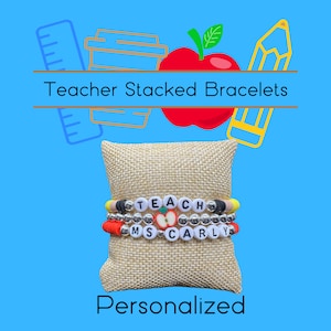 May include: Teacher Stacked Bracelets with the words "TEACH" and "MS CARLY" on them. The bracelets are on a small beige cushion. The image has a blue background with a red apple, a yellow pencil, a brown coffee cup, and a blue ruler.