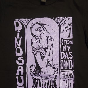 May include: A black t-shirt with a purple print of a concert poster for Dinosaur Jr. The poster features a drawing of a person with their arms raised, and the text "Dec 7 & From N.Y. Das Damen Sheehan's Cafe".