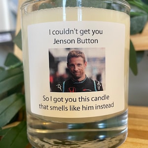 Op de afbeelding: Een glazen kaarsvaas met een wit label waarop staat "I couldn't get you Jenson Button So I got you this candle that smells like him instead". Het label bevat ook een foto van Jenson Button in een racepak.