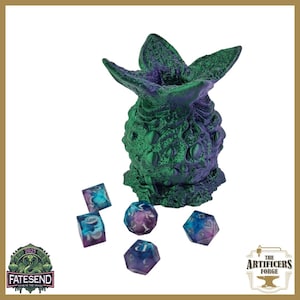 May include: A green and purple dice tower with a textured, organic design, resembling a plant or creature. Several polyhedral dice in shades of blue, purple, and white are scattered around the tower. The image includes logos for "Fatesend" and "The Artificers Forge."