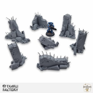 Peut inclure: Ensemble de ruines de bâtiments miniatures grises avec des tiges métalliques, et une figurine bleue et argentée. Les ruines sont de formes et de tailles variées, suggérant un environnement de guerre. Le logo "TXARLI FACTORY" est visible.