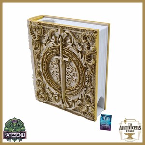 Puede incluir: Un libro dorado detallado con tallas ornamentadas y un emblema de espada en la portada. El libro tiene páginas con bordes blancos y una pequeña tarjeta colorida al lado. La portada del libro está intrincadamente diseñada.