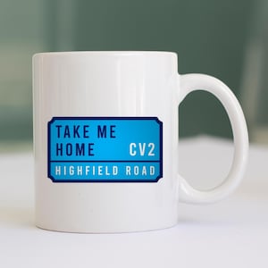 May include: White ceramic mug with a blue and black design. The design says "Take Me Home" and "CV2 Highfield Road".