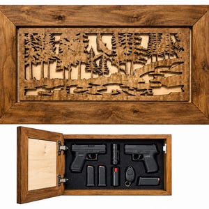May include: A rectangular wooden wall cabinet with a laser-cut forest scene on the front door. The interior features black foam padding holding two black semi-automatic pistols, three magazines, a flashlight, and a small black key fob.