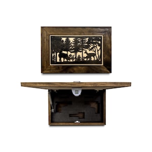May include: A rectangular wooden wall-mounted safe with a dark brown finish. The front panel features a laser-cut forest scene with deer silhouettes. The unit is shown open, revealing a dark gray foam-lined interior and a digital keypad lock.