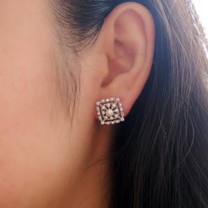 May include: Silver square earrings with a pearl in the center and a diamond-like design around the pearl.