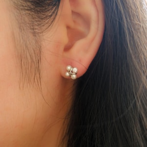 May include: A pair of silver earrings with four small white pearls arranged in a flower shape.