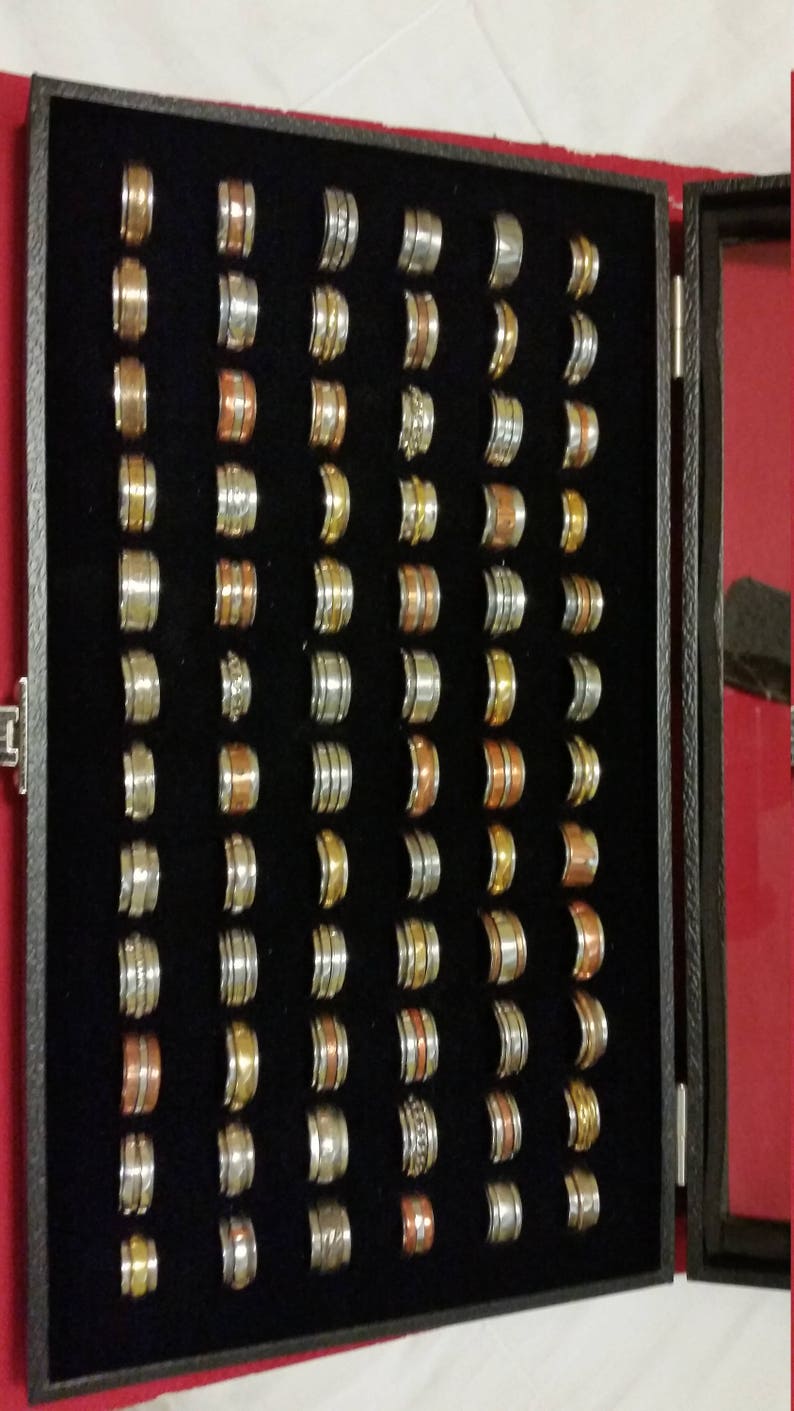 May include: A black velvet-lined box filled with a variety of silver, gold, and copper spinner rings. The rings are arranged in rows and columns, and each ring has a unique design.