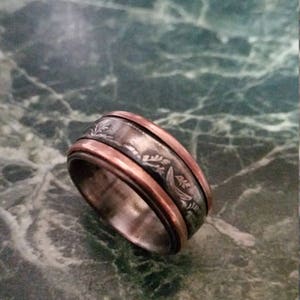 May include: A silver and copper ring with a floral design. The ring is on a green marble surface.