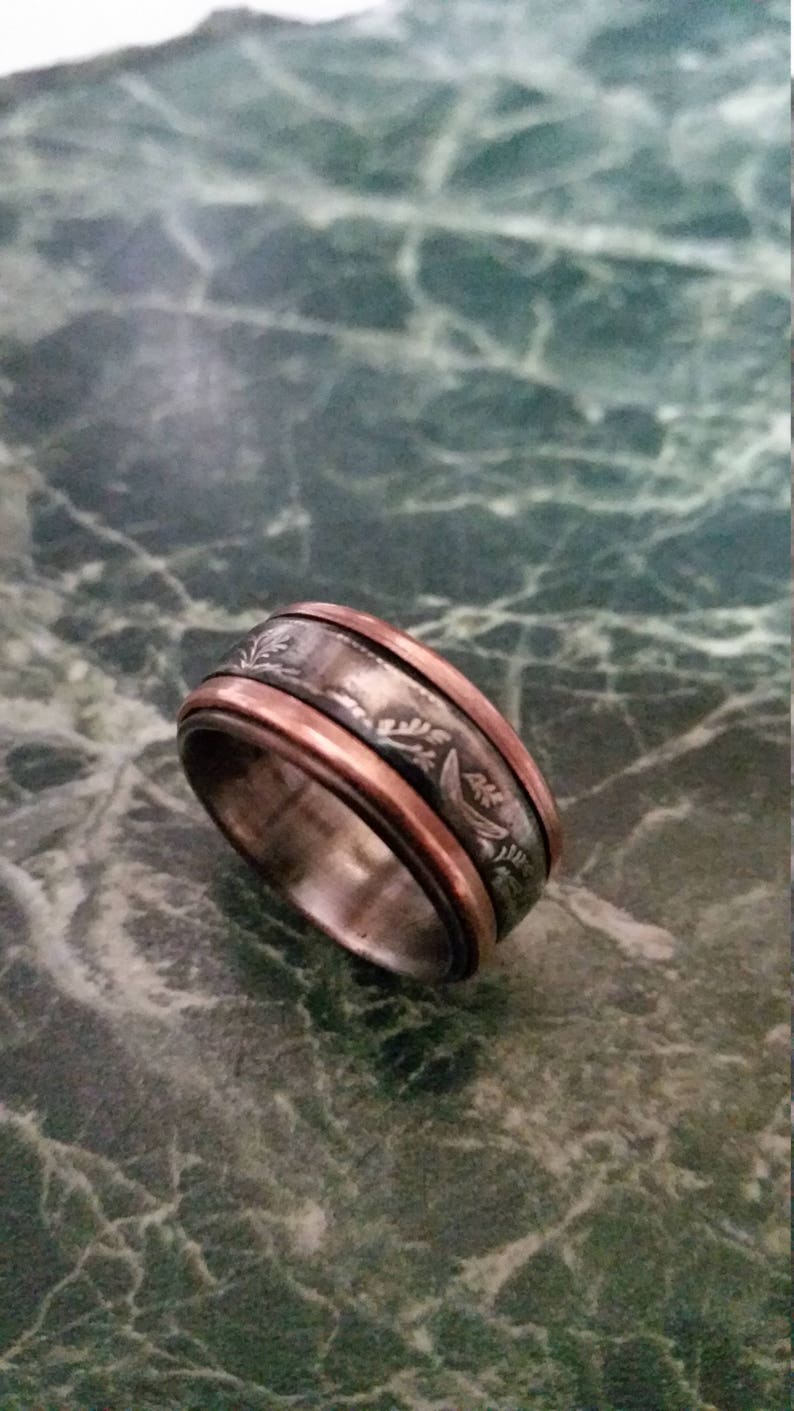 May include: A silver and copper ring with a floral design. The ring is on a green marble surface.
