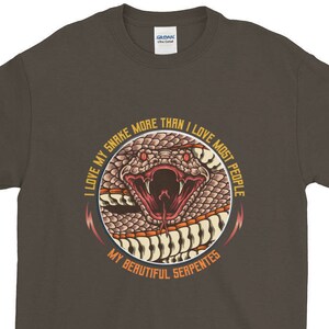 Op de afbeelding: Een donkerbruin T-shirt met een afbeelding van een slang met de tekst "Ik hou meer van mijn slang dan van de meeste mensen. Mijn prachtige slangen."
