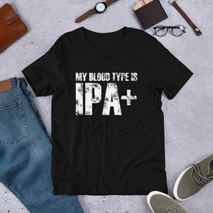 Può includere: Maglietta nera con una grafica bianca usurata che dice "My blood type is IPA+"