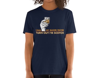 Puede incluir: Una camiseta azul marino con un gráfico de una mano sosteniendo un vaso de whisky. El texto en la camiseta dice "I had my blood tested turn out I'm scotch".