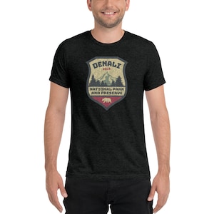 May include: A dark heather grey t-shirt with a vintage-style graphic of a shield with the text "Denali National Park and Preserve" and the year "2019".