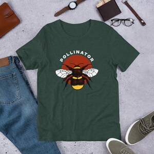 May include: A dark green t-shirt with a graphic of a bumblebee in front of a red sun. The text "POLLINATOR" is written in a white circle around the sun.
