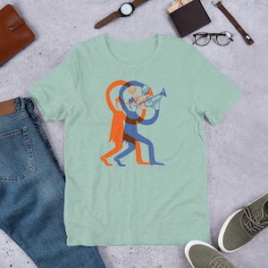 Könnte beinhalten: Ein hellgrünes T-Shirt mit einem Motiv einer Person, die Trompete spielt. Die Person ist in einem blau-orangenen Farbschema dargestellt.