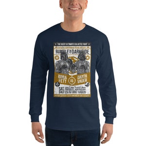 May include: A navy blue long-sleeve t-shirt with a vintage-style poster design featuring a boxing match between Boba Fett and Darth Vader. The poster text reads "The Most Ultimate Galactic Fight" and "Rumble in Darkside".