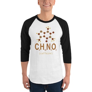 Op de afbeelding: Wit en zwart baseballshirt met een bruine cafeïnemolecuulafbeelding. De afbeelding bevat de chemische formule C8H10N4O2 en het woord "caffeine" tussen haakjes. Het shirt heeft zwarte mouwen en een witte body.