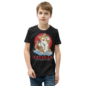 May include: Black youth t-shirt featuring a cartoon cat holding a fish. The cat is in front of a red sun and waves. The text "CATZILLA THE MOST DANGEROUS TITAN IN HISTORY" is below the cat.
