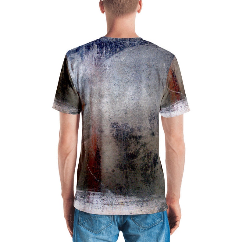 Puede incluir: Una camiseta gris, azul y &oacute;xido con un dise&ntilde;o abstracto. La camiseta tiene cuello redondo y mangas cortas.