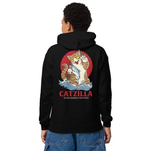 May include: Black hoodie featuring a graphic of a cartoon cat holding a fish in front of a red sun and blue waves. The text "CATZILLA THE MOST DANGEROUS TITAN IN HISTORY" is printed below the graphic.