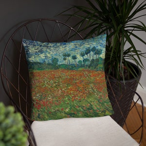 Puede incluir: Una almohada con una pintura vibrante e impresionista de un campo de amapolas rojas con una fila de árboles en el fondo. El cielo es azul claro con nubes blancas.