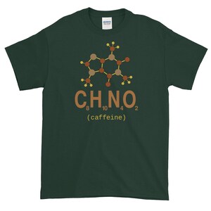 Op de afbeelding: Een donkergroen T-shirt met een bruine en gele chemische structuur van cafeïne, met de chemische formule C8H10N4O2 en het woord "(cafeïne)" eronder.