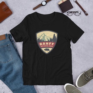 May include: Black t-shirt with a vintage-style graphic of a mountain range and a bear. The graphic is in a shield shape with the text "Banff National Park".