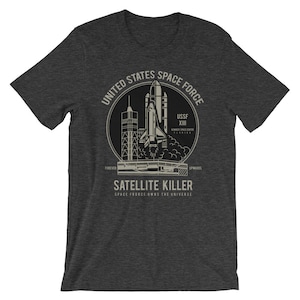 Könnte beinhalten: Ein dunkel-helles graues T-Shirt mit einem Grafikdruck einer Raumfähre, die von einem Weltraumzentrum abhebt. Die Grafik enthält den Text "United States Space Force", "USSF XIII", "Kennedy Space Center", "Florida", "Forever Upwards", "Satellite Killer" und "Space Force Owns The Universe".