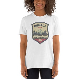 May include: White t-shirt with a vintage-style graphic of a shield with the text "DENALI 2019 NATIONAL PARK AND PRESERVE" and a mountain scene inside the shield.